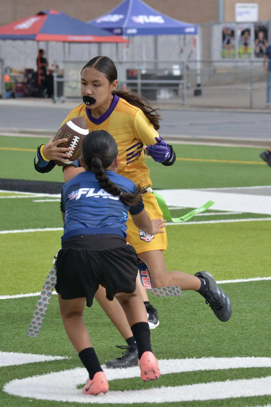 Girls division ball carrier in an NFL Flag uniform evading a flag pull