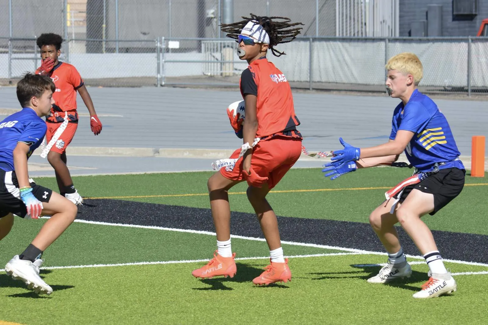 Receiver in an official NFL FLAG jersey hauling in a catch mid-air between two defenders at Mt. View