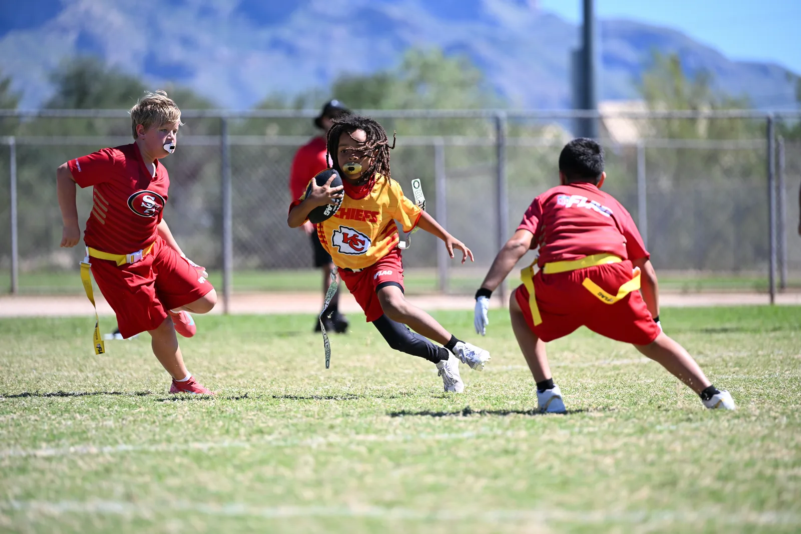 Chiefs ball carrier cutting between two 49ers defenders with the Catalina Mountains behind the field