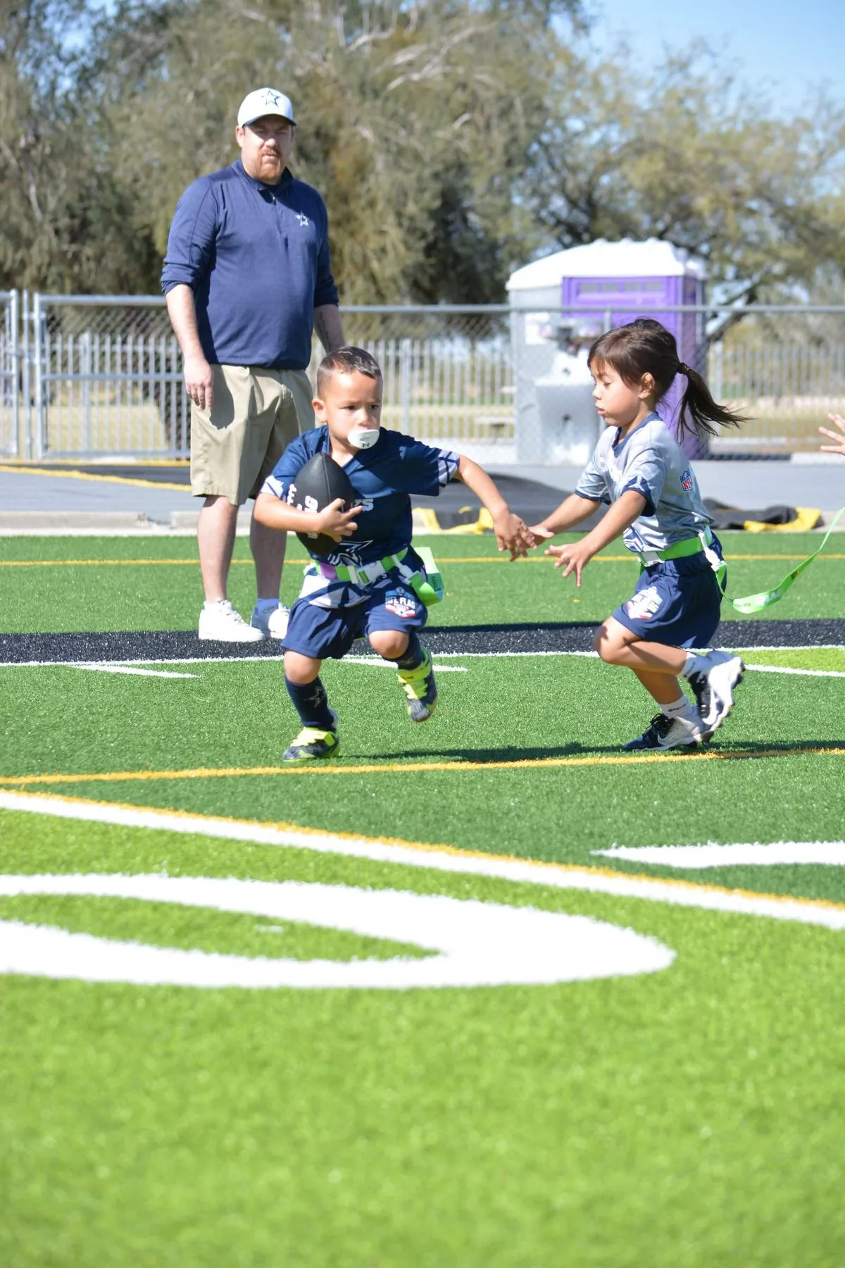 6U players executing a handoff while the referee watches