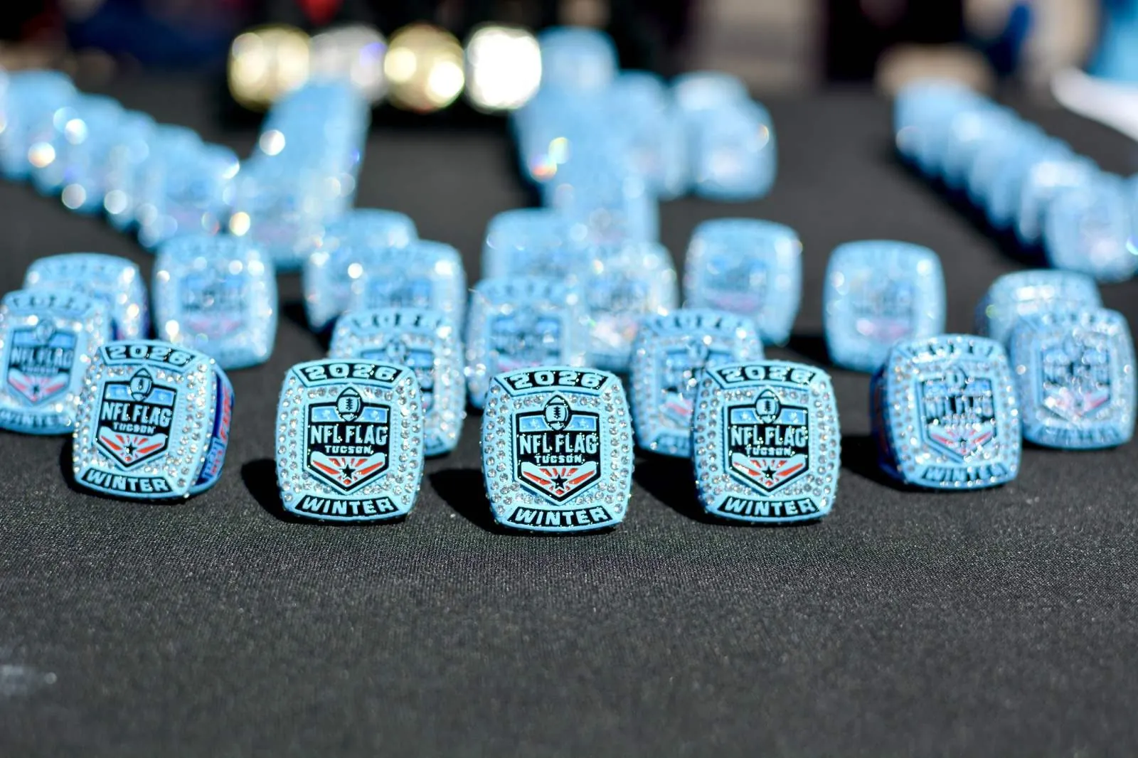 Rows of NFL Flag Tucson Winter 2026 championship rings laid out on a table